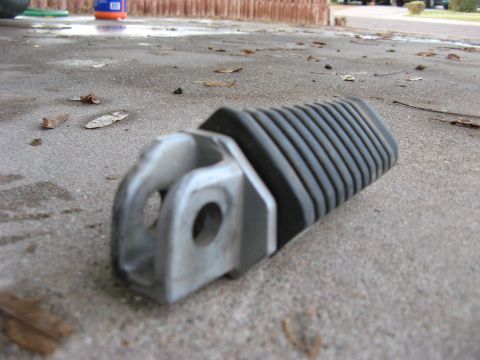 2007 Kawasaki Ninja - A close-up view of a motorcycle foot peg resting on a wet concrete surface with scattered leaves.