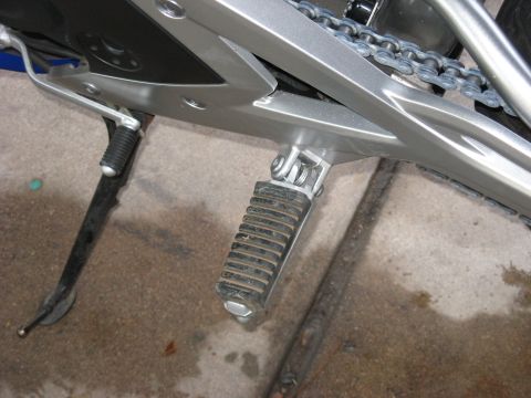 2007 Kawasaki Ninja - Close-up view of a motorcycle's footpeg and drive chain against a concrete surface.
