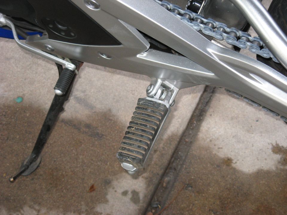 Motorcycle's silver frame, black footpeg, and chain are visible from a low angle