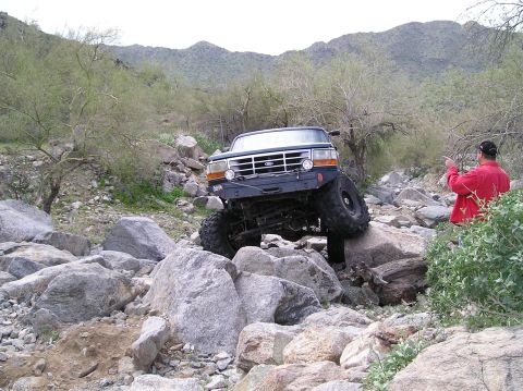 1986 Toyota Hilux - A Ford Bronco tackles a challenging rocky terrain with a person observing.