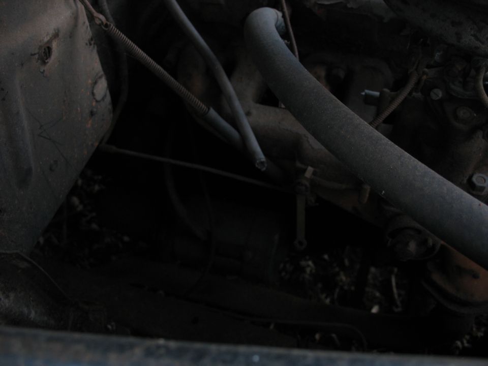 Dim engine bay with rusty manifold, hoses and wiring