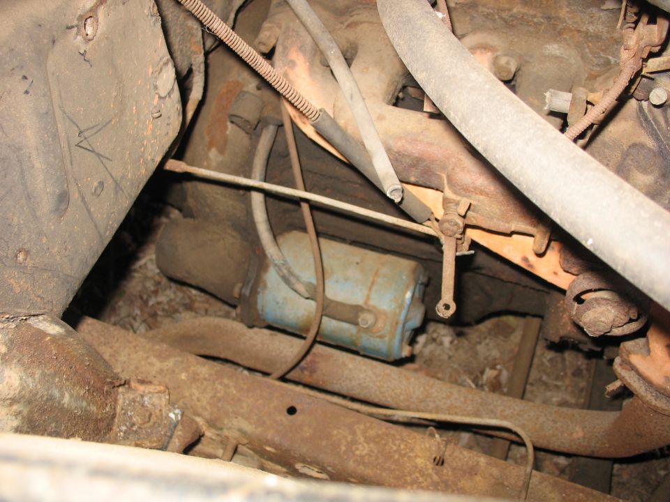Blue canister-shaped part amid rusty undercarriage frame and exhaust components