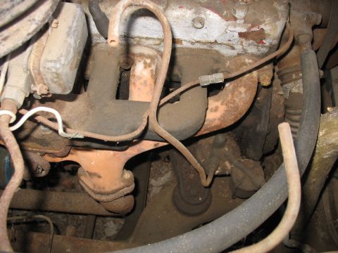 1952 Ford Panel Van - Close-up view of an engine's exhaust manifold, showing rusty pipes and various hoses connected to the engine block.