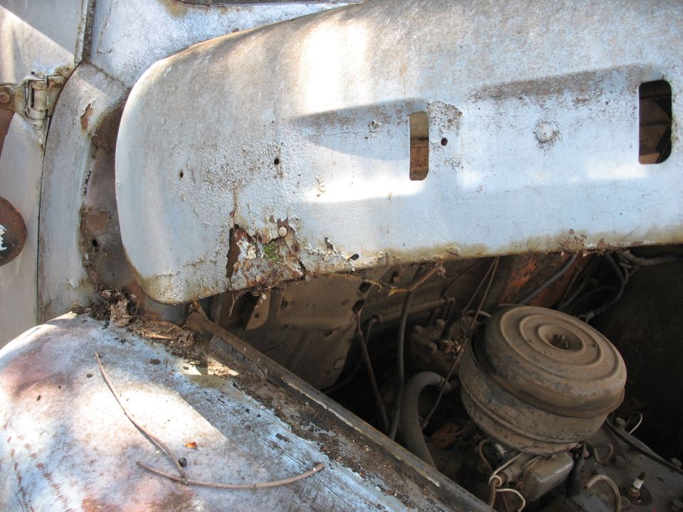 Rusty fender and engine bay of old vehicle with round air cleaner and peeling paint
