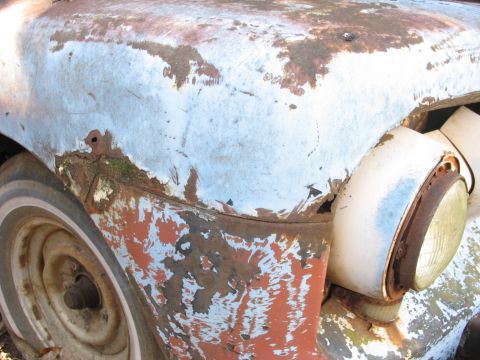 1952 Ford Panel Van - The weathered exterior of an old vehicle shows significant rust and peeling paint, revealing multiple layers of color.
