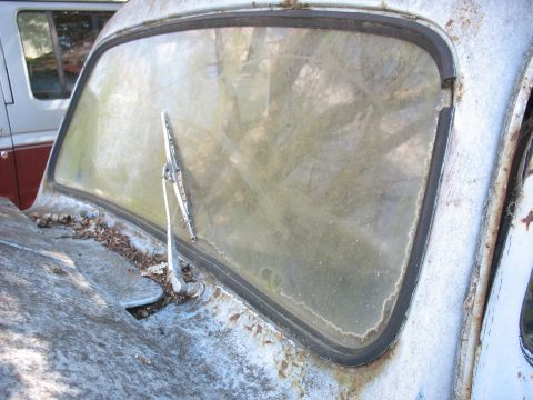 1952 Ford Panel Van - The front of a dilapidated van, showing a dirty windshield and worn hood, with another vehicle visible in the background.