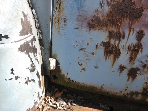 1952 Ford Panel Van - Detail of heavily rusted and peeling paint on a metal surface, showing signs of wear and age.