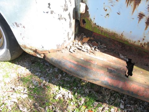 1952 Ford Panel Van - The lower body panel of an old vehicle shows significant rust and damage, with debris collected in the wheel well.