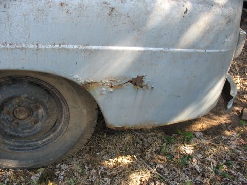 1952 Ford Panel Van - A light blue van's rear fender shows significant rust and damage near the wheel.