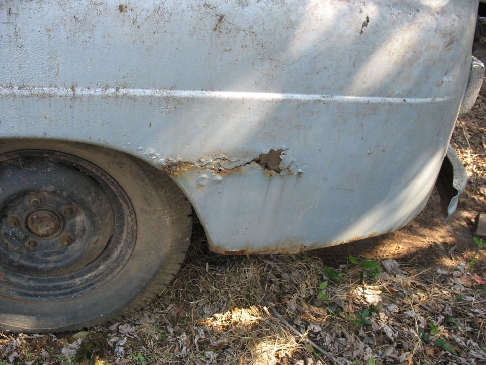 Rusted rear quarter panel and steel wheel of a faded blue vehicle parked outdoors