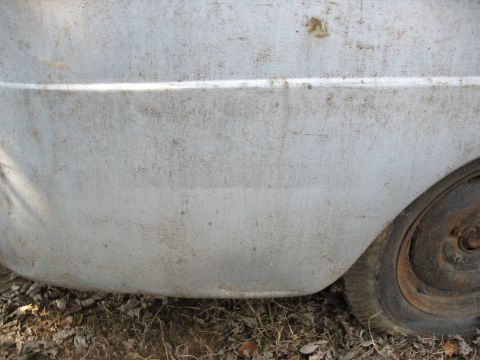1952 Ford Panel Van - Close-up of a weathered panel van's rear side, revealing its aged condition and a rusty wheel.