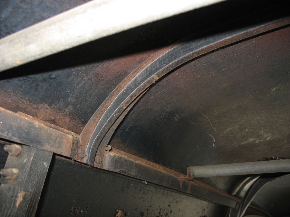 Rusty black curved sheet-metal fender edge with bolted seams and metal rod