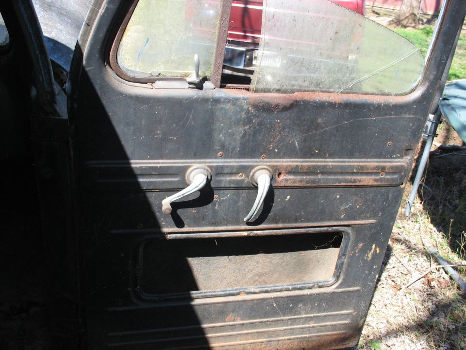 Weathered black door panel with two chrome handles from a vintage panel van