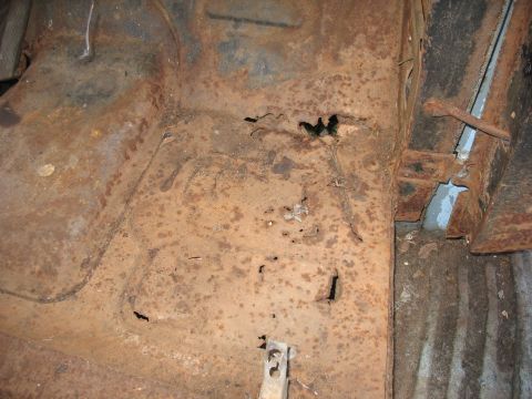 1952 Ford Panel Van - Close-up of a heavily rusted vehicle floor pan with multiple rust-through holes and severe corrosion, showing the original stamped contours…