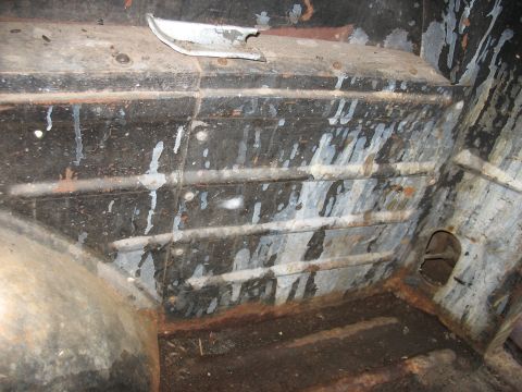 1952 Ford Panel Van - Inside the cargo area of a vintage panel van, showing the ribbed wood-and-metal floor strips covered in paint splatter and surface rust, a…