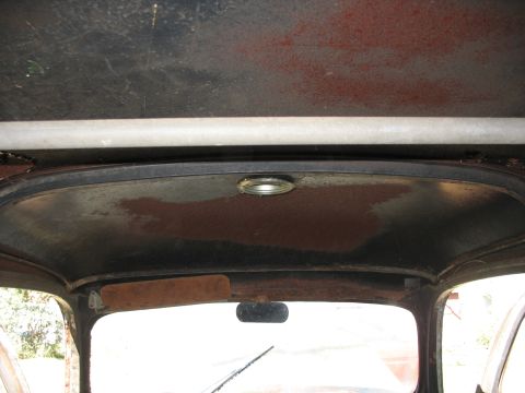 1952 Ford Panel Van - Interior view looking up at the bare-metal roof and headliner of an old vehicle cab, showing surface rust, a round dome light, and the rear…
