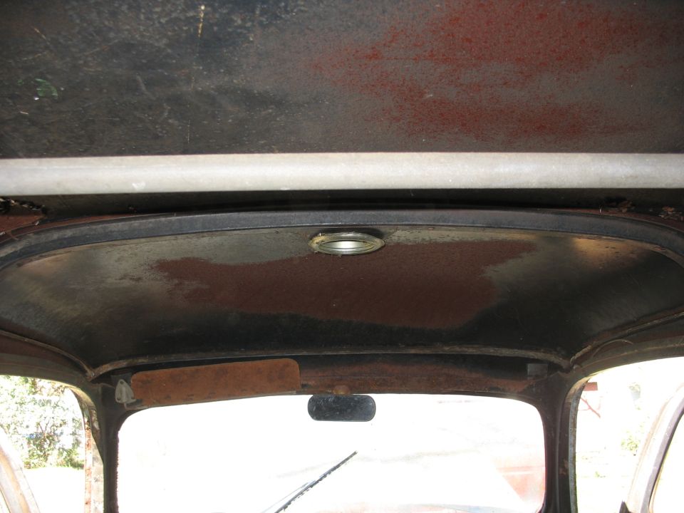 Interior roof of an old vehicle cab, bare rusty metal with a round dome light and rear window.