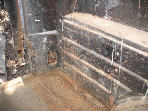 1952 Ford Panel Van - Interior of a gutted, weathered vehicle body shot from above, showing the bare ribbed rear cargo/wheelhouse panel and floor with peeling bl…
