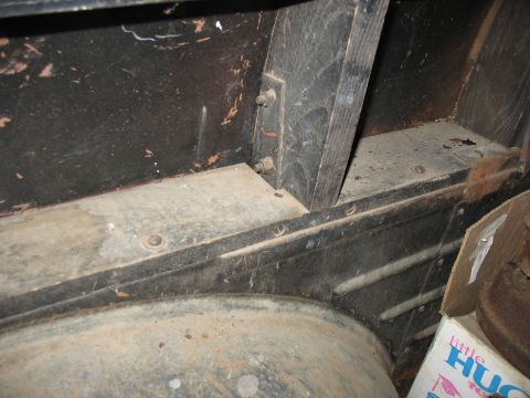 1952 Ford Panel Van - Close-up inside a bare vehicle body showing weathered wooden floor framing bolted to a black painted steel body panel, with a wooden sill b…