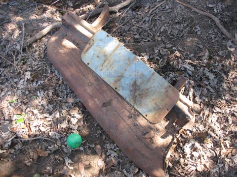 1952 Ford Panel Van - A rusted, curved sheet-metal automotive body panel lying on leaf-covered ground in the woods, with a bolted-on rectangular steel cover plat…