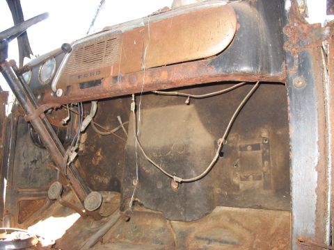 1952 Ford Panel Van - Stripped, heavily rusted cab interior of a vintage Ford truck shot from the passenger side, showing the metal dash with FORD lettering, spe…
