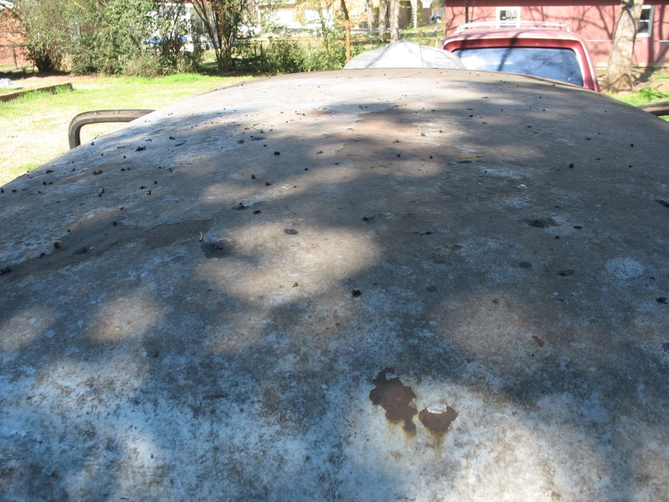 Bare-metal roof of an old vehicle stripped for restoration with rust spots and sanding marks