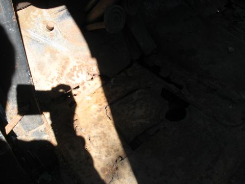 1952 Ford Panel Van - Harsh-sunlight interior shot down into the stripped cab floor of an old vehicle, showing surface-rusted and cracked floor pan sheet metal,…