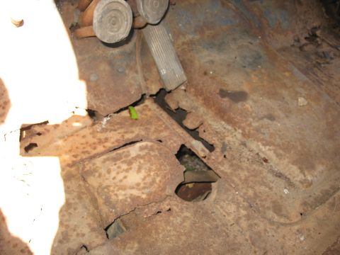 1952 Ford Panel Van - Interior floor-pan view of an old vehicle showing severe rust-through, with jagged perforations and holes opening to the ground below. The…