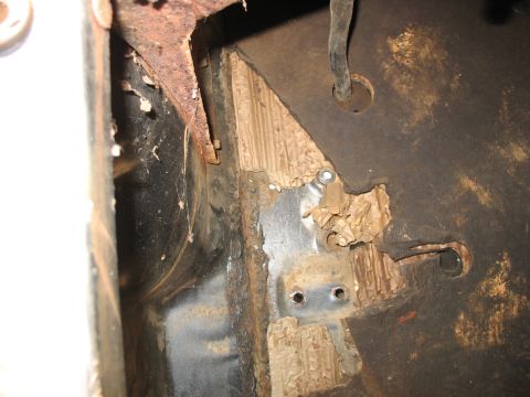 1952 Ford Panel Van - Close-up inside a stripped cab looking down at a bare steel floor pan and inner rocker, with flaking tan sound-deadening pad, surface rust…