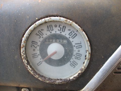 1952 Ford Panel Van - Close-up of a vintage round speedometer set in a weathered gray dash, marked 0 to 90 mph with a red needle at rest and an odometer reading…