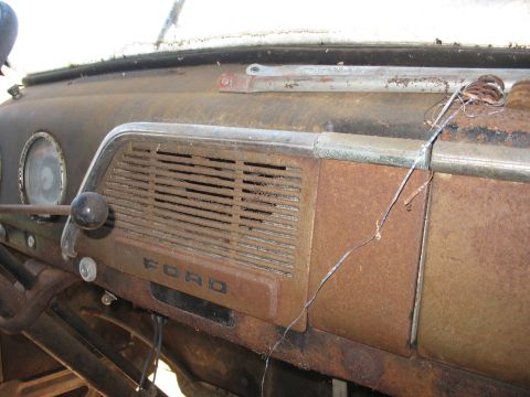 1952 Ford Panel Van - Close-up of the heavily surface-rusted painted-steel dashboard of an early-1950s Ford truck, showing the louvered speaker grille with embos…