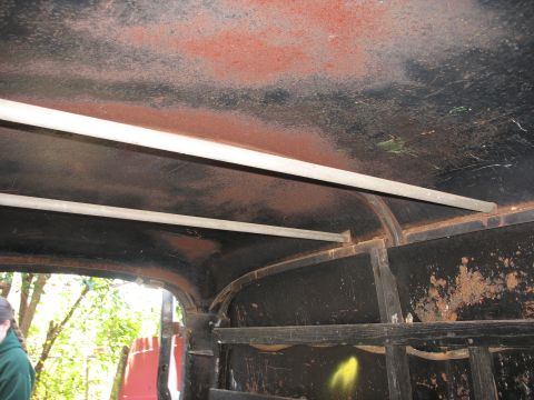 1952 Ford Panel Van - Looking up into the bare interior roof of an unrestored panel truck body, with surface rust and orange primer showing through flaking black…