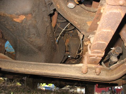 1952 Ford Panel Van - Underside view of a heavily rusted vehicle chassis showing the boxed frame rail, a rusty multi-leaf spring pack with U-bolts, and grimy sus…