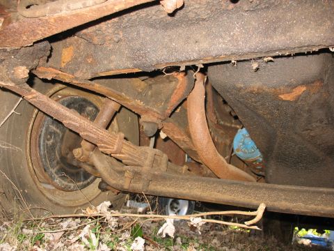 1952 Ford Panel Van - Low-angle underside shot of a rusted vintage truck's rear frame rail and leaf-spring suspension, with a corroded exhaust pipe running back…