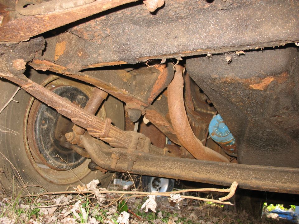 Rusted underside of vintage truck showing leaf spring, exhaust pipe and blue shock absorber