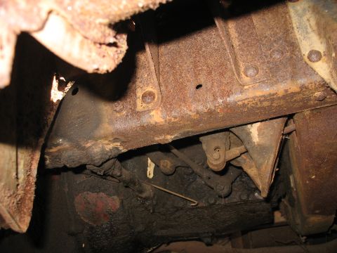 1952 Ford Panel Van - Tight underbody shot of a heavily rusted ladder frame rail and riveted crossmember, with surface scale, flaking metal and a rust hole visib…