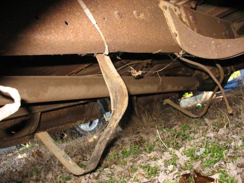 1952 Ford Panel Van - Undercarriage view of a heavily rusted vehicle frame, showing corroded frame rails, a curved steel bracket and driveline components. The ve…