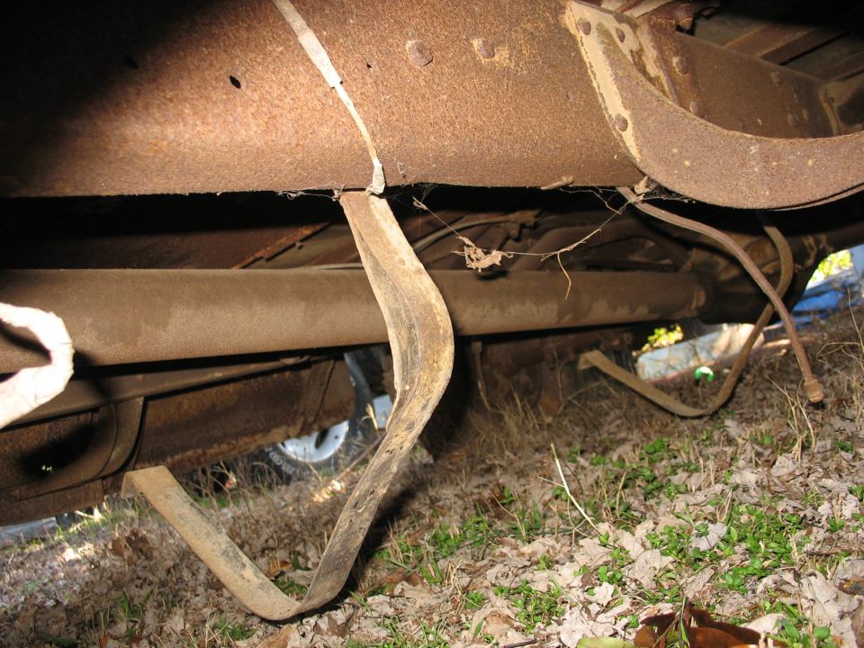 Rusted undercarriage and frame rails of an old vehicle over grass and leaves