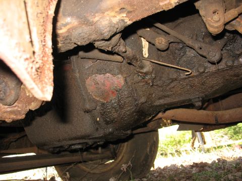 1952 Ford Panel Van - Underside close-up of a heavily grease-caked and rusted transmission or bellhousing area on an old vehicle parked outdoors on leaf litter,…
