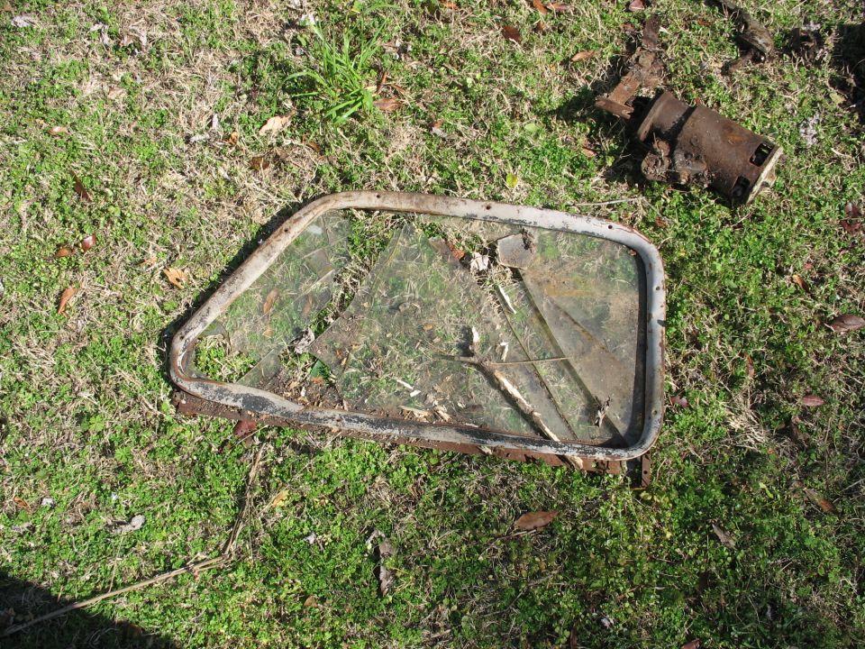 Rusty vehicle door window frame with broken glass lying on grass