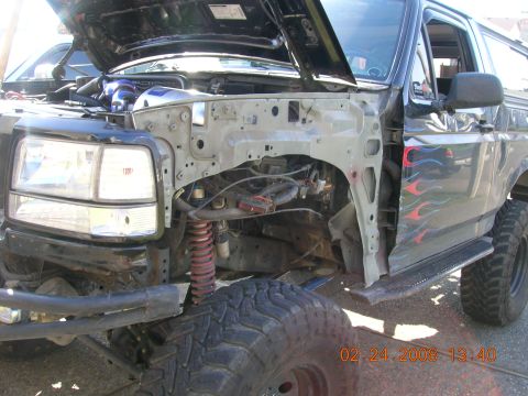 1996 Ford Bronco - The front fender of a black 1996 Ford Bronco is removed, revealing the engine bay and suspension components. Flames are visible on the side…