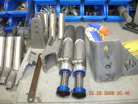 1996 Ford Bronco - Various metal parts, likely for vehicle suspension, are organized in blue bins and laid out on a surface.