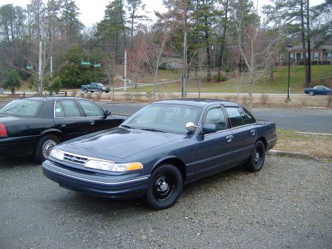 2001 Ford Crown Victoria - Two Ford Crown Victorias are parked outside on a gravel lot with trees in the background.