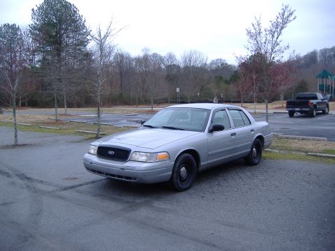 2001 Ford Crown Victoria - A silver 2001 Ford Crown Victoria sedan is parked in an outdoor lot with a pickup truck in the background.