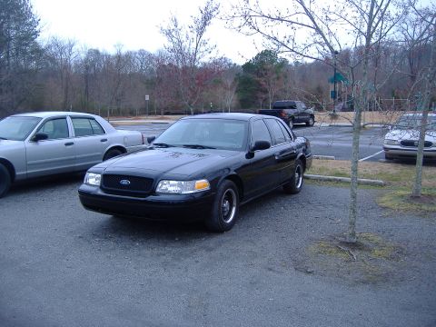 2001 Ford Crown Victoria - A black 2001 Ford Crown Victoria sedan is parked in a lot with other vehicles visible.