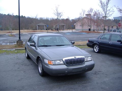 2001 Ford Crown Victoria - A gray Mercury Grand Marquis is parked in a lot with a dark sedan in the background.