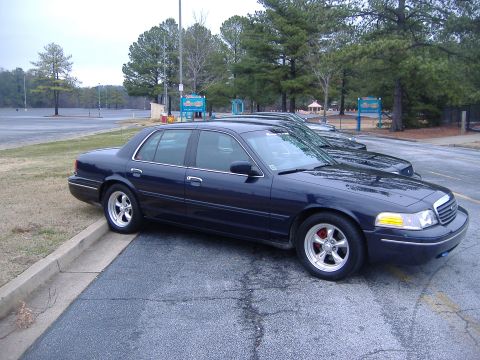2001 Ford Crown Victoria - A dark blue 2001 Ford Crown Victoria is parked next to another vehicle in an outdoor lot.