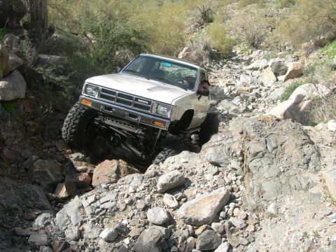 1986 Toyota Hilux - A white 1986 Toyota Hilux navigates a challenging rocky terrain during an off-road excursion.