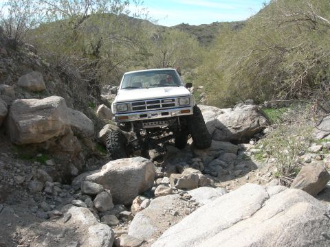 1986 Toyota Hilux - Pickup truck navigating a challenging rocky trail in a desert landscape.