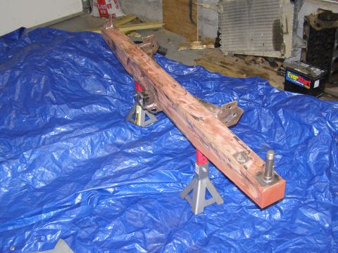 1993 Ford Bronco - A vehicle frame component is supported by jack stands on a blue tarp, with a radiator and battery in the background.